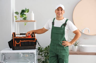 Tuvaletteki çamaşır makinesinde bir çanta dolusu alet edevat taşıyan erkek tesisatçı.