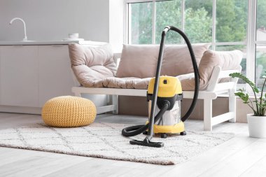 Evdeki beyaz kanepenin yanındaki halının üzerinde modern elektrikli süpürge.