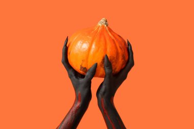 Turuncu arka planda pençeleri ve balkabağı olan kara cadı elleri. Cadılar Bayramı