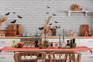 Cadılar Bayramı dekorlu yemek masası ve mutfakta yanan mumlar.