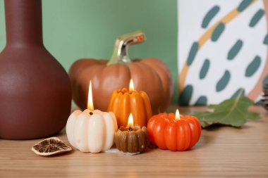 Evdeki yeşil duvarın yakınındaki masada balkabağı şeklinde mumlar ve orman çıkıntıları yakıyor.