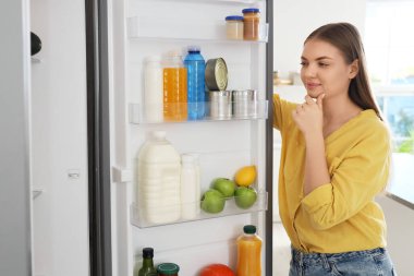 Mutfaktaki açık buzdolabının yanında düşünceli bir genç kadın.