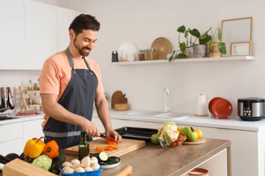 Yakışıklı sakallı adam mutfakta dolma biber kesiyor.