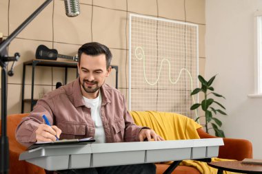 Müzik stüdyosunda sentezleyici çalarken notlar yazan genç, mutlu erkek besteci.