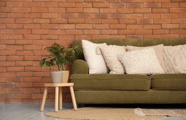 Dekoratif yastıklı yeşil kanepe ve odada tuğla duvarın yanında bitki.