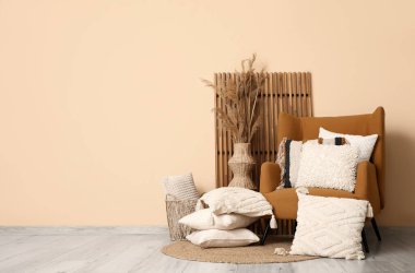 Dekoratif yastıklı koltuklar ve bej duvarın yanında otlar.