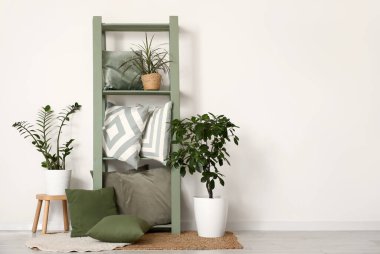 Beyaz duvarın yanında yastıklı ve çiçekli raf ünitesi.