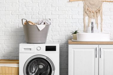 Modern çamaşır makinesi, çamaşır sepetleri ve banyo lavabosu olan çekmeceler.