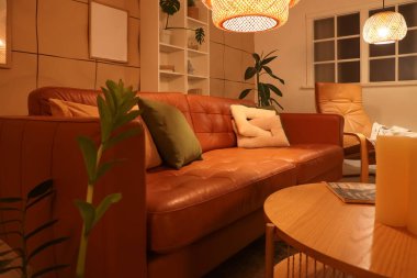 Kahverengi kanepesi, sehpası, mumları ve parlayan lambası olan şık bir oturma odası.