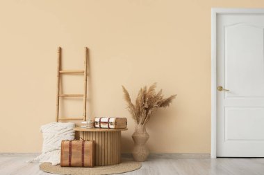 Odada bej duvarın yanında merdiven, masa ve klasik bavullar.