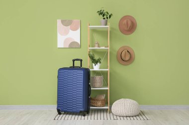 Mavi bavul ve raflarda yeşil duvarın yanında pouf var.