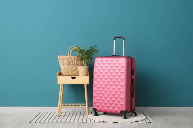 Mavi duvarın yanında çiçekli ve bavullu bir masa.