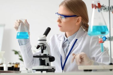 Matarası ve mikroskobu olan kadın bilim adamı laboratuarda çalışıyor.