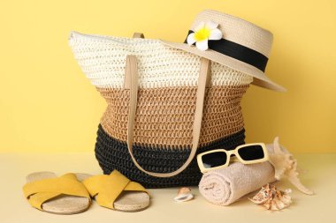 Hasır çanta, deniz kabukları ve sarı arka planda plaj aksesuarları, yakın plan.