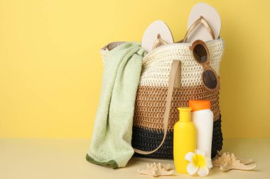 Hasır çanta, güneş kremi şişeleri, çiçek ve plaj aksesuarları sarı arka planda, yakın plan