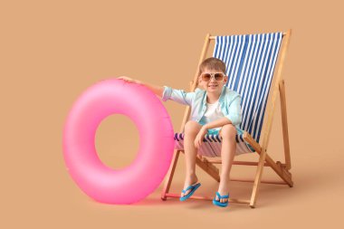 Kahverengi arka planda şezlongda oturan şişme yüzüklü şirin küçük çocuk. Seyahat kavramı