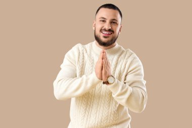 Minnettar genç adam avuçlarını birbirine bastırıyor ve bej arka planda gülümsüyor.