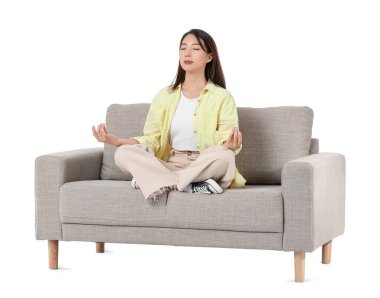 Genç Asyalı kadın beyaz arka planda gri koltukta meditasyon yapıyor.