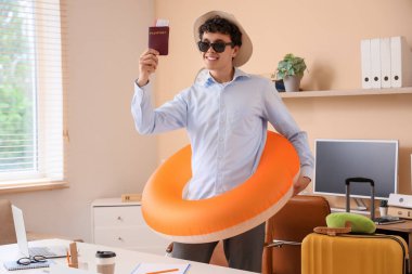 Yüzme yüzüğü ve pasaportu olan genç işadamı yaz tatilini ofisinde bekliyor.