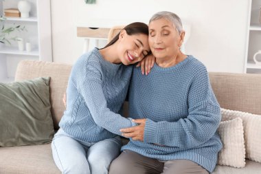 Mutlu genç bir kadın ve büyükannesi evde kanepede sarılıyorlar.