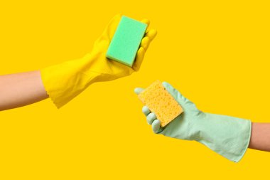 Sarı arka planda sünger tutan lastik eldivenli eller.