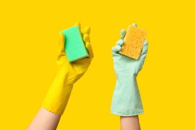 Sarı arka planda sünger tutan lastik eldivenli eller.