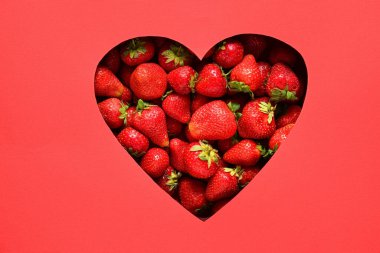 Kırmızı kağıttaki kalp şeklindeki delikten görülebilen bir sürü tatlı çilek.