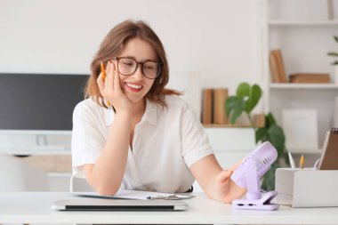 Ofiste çalışan genç bayanın masasındaki küçük elektrikli vantilatör.