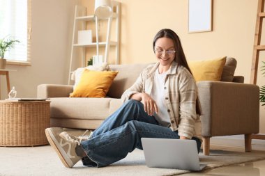 Genç kadın evde dinlenirken dizüstü bilgisayar kullanıyor.