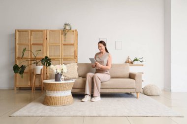 Tabletli genç bir kadın evdeki kanepede dinleniyor.