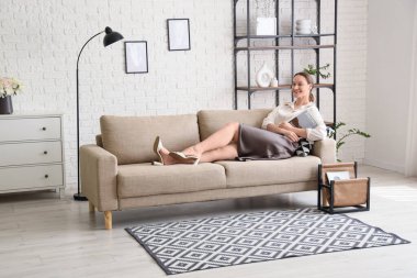 Dergideki genç kadın işten sonra evdeki kanepede dinleniyor.