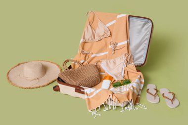 Yeşil arka planda şık mayo ve plaj aksesuarları olan valizi aç, yakın plan.