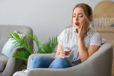 Evinde diş ağrısı çeken, çözünmüş tabletle bir bardak suya atılmış genç bir kadın.