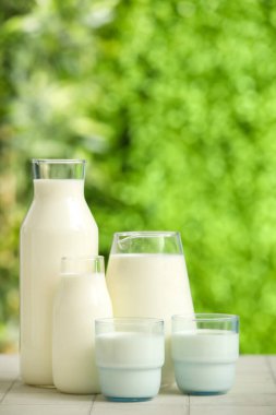 Bardaklar ve şişeler beyaz fayans masasında taze süt.