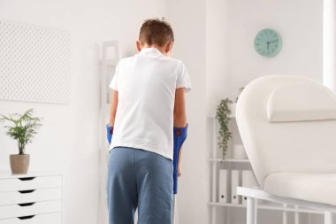 Koltuk değnekli yaralı bir çocuk klinikte yürüyor.