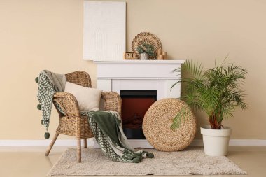 Odanın içi şömine ve battaniyeyle bej duvarın yanındaki hasır koltukta.