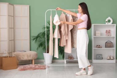 Elbise rafının yanındaki güzel genç kadın mağazada elbise seçiyor.