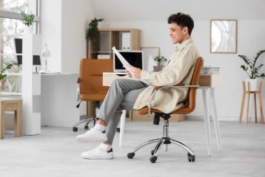 Genç adam ofiste gazete okuyor.