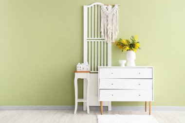 Katlanan ekran, klozet ve vazoda mimoza çiçekleri olan odanın içi