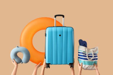 Plaj aksesuarları ve bej arka planda valizi olan kadın eller.