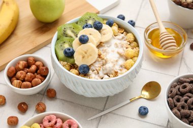 Yoğurtlu sağlıklı tahıl kasesi, beyaz fayanslı taze meyve ve fındık, yakın plan.