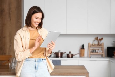 Mutfakta tablet bilgisayar kullanan genç bir kadın.