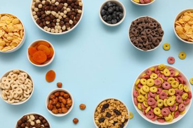 Farklı lezzetli tahıllar, böğürtlenler, kuru meyveler ve mavi arka planda fındıklı kaselerden yapılmış çerçeve.