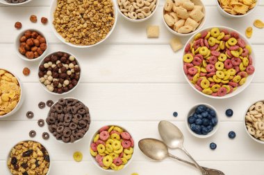 Farklı lezzetli tahıllar, böğürtlenler ve beyaz ahşap arka planda fındıklı kaselerden yapılmış çerçeve.