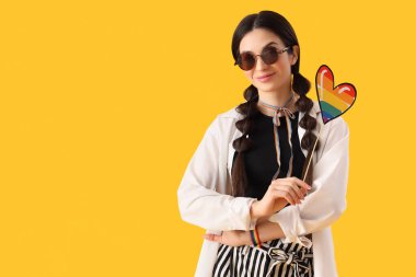 Sarı arka planda gökkuşağı kalpli güzel bir genç kadın. LGBT kavramı