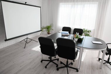 Modern ofiste masa, ev bitkileri ve projektör ekranlı konferans salonu.
