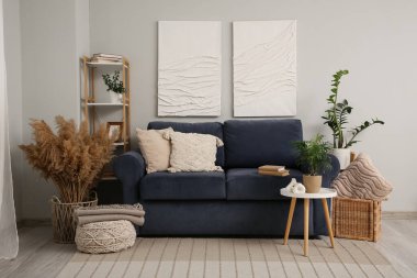 Mavi kanepe, içinde otlar olan sepet ve oturma odasının iç tarafındaki beyaz duvarın yanında puf.