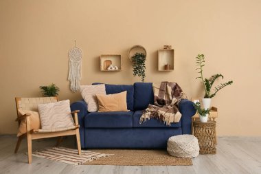 Oturma odasının iç tarafındaki bej duvarın yanında mavi kanepe, puf ve koltuk.