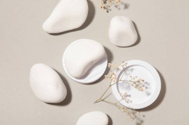 Beyaz çakıl taşlı dekoratif podyumlar ve gri arka planda alçıtaşı çiçekleri