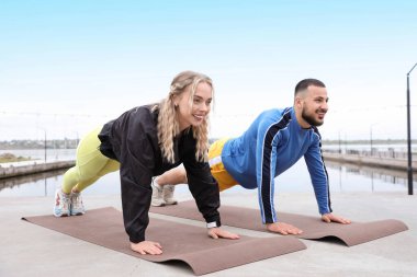 Sportif genç çift nehir kıyısında kalas yapıyor.